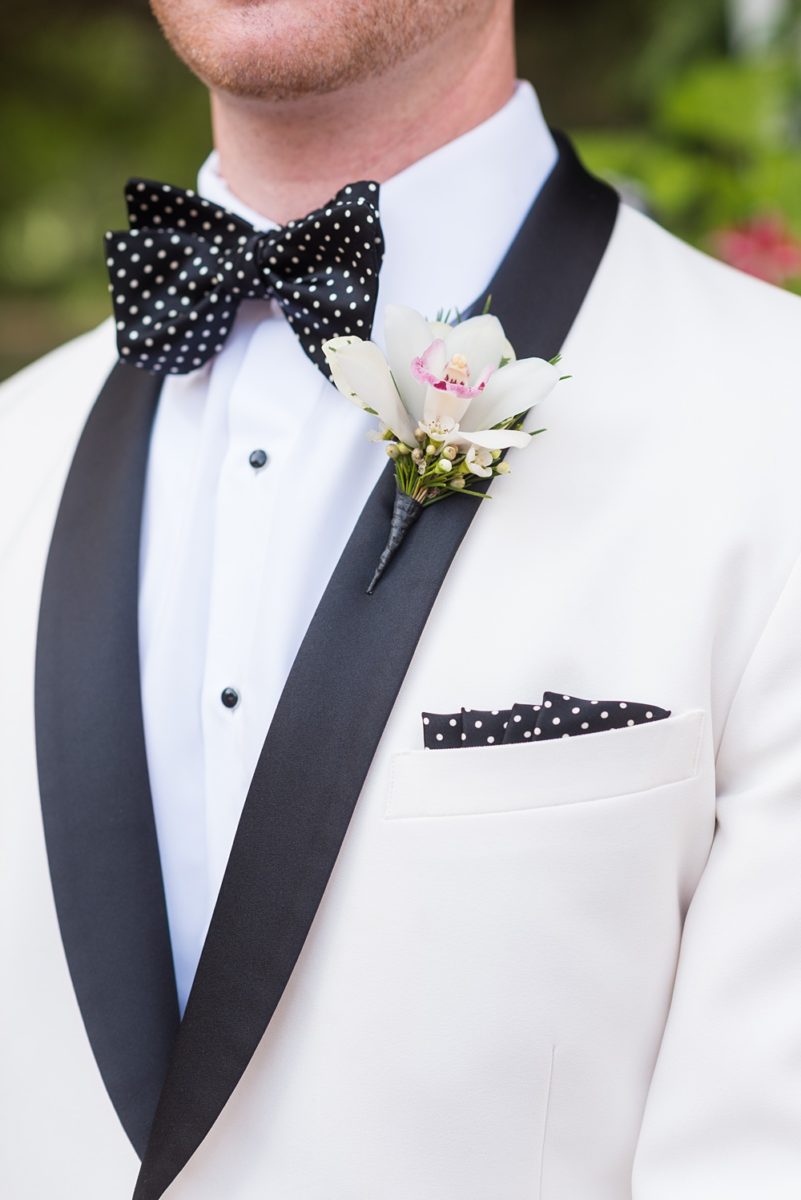Photos of the groom's white tuxedo with black lapel and orchid boutonniere on Long Island by Mikkel Paige Photography for her East Wind wedding in Wading River, NY. The wedding venue has a beautiful outdoor ceremony area and pretty indoor reception space. #mikkelpaige #newyorkweddingphotographer #longislandweddingvenue #summer #weddingdetails #whitetuxedo #groomstyle #orchidboutonniere