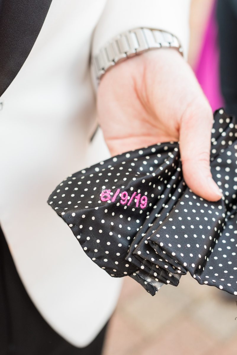 Detail pictures of the groom's black and white pocket square with their wedding date embroidered on it in hot pink thread. Photos by Mikkel Paige Photography at an East Wind wedding in Wading River, NY on Long Island. The wedding venue has a beautiful outdoor ceremony area and pretty indoor reception space. #mikkelpaige #newyorkweddingphotographer #longislandweddingvenue #weddingdetails #pocketsquare