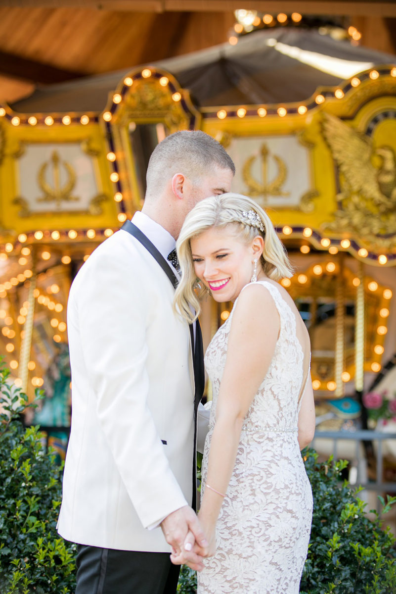 Photos of the bride and groom by a carousel by Mikkel Paige Photography at an East Wind wedding in Wading River, NY on Long Island. The wedding venue has a beautiful outdoor ceremony area and pretty indoor reception space. #mikkelpaige #newyorkweddingphotographer #longislandweddingvenue #summerbride #laceweddinggown #bridestyle #BrideandGroom