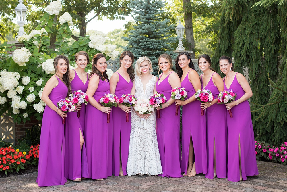 Photos of the bride and bridesmaids in purple gowns by Mikkel Paige Photography at an East Wind wedding in Wading River, NY on Long Island. The wedding venue has a beautiful outdoor ceremony area and pretty indoor reception space. #mikkelpaige #newyorkweddingphotographer #longislandweddingvenue #summerbride #laceweddinggown #bridestyle #purplewedding #bridesmaids #bridalparty