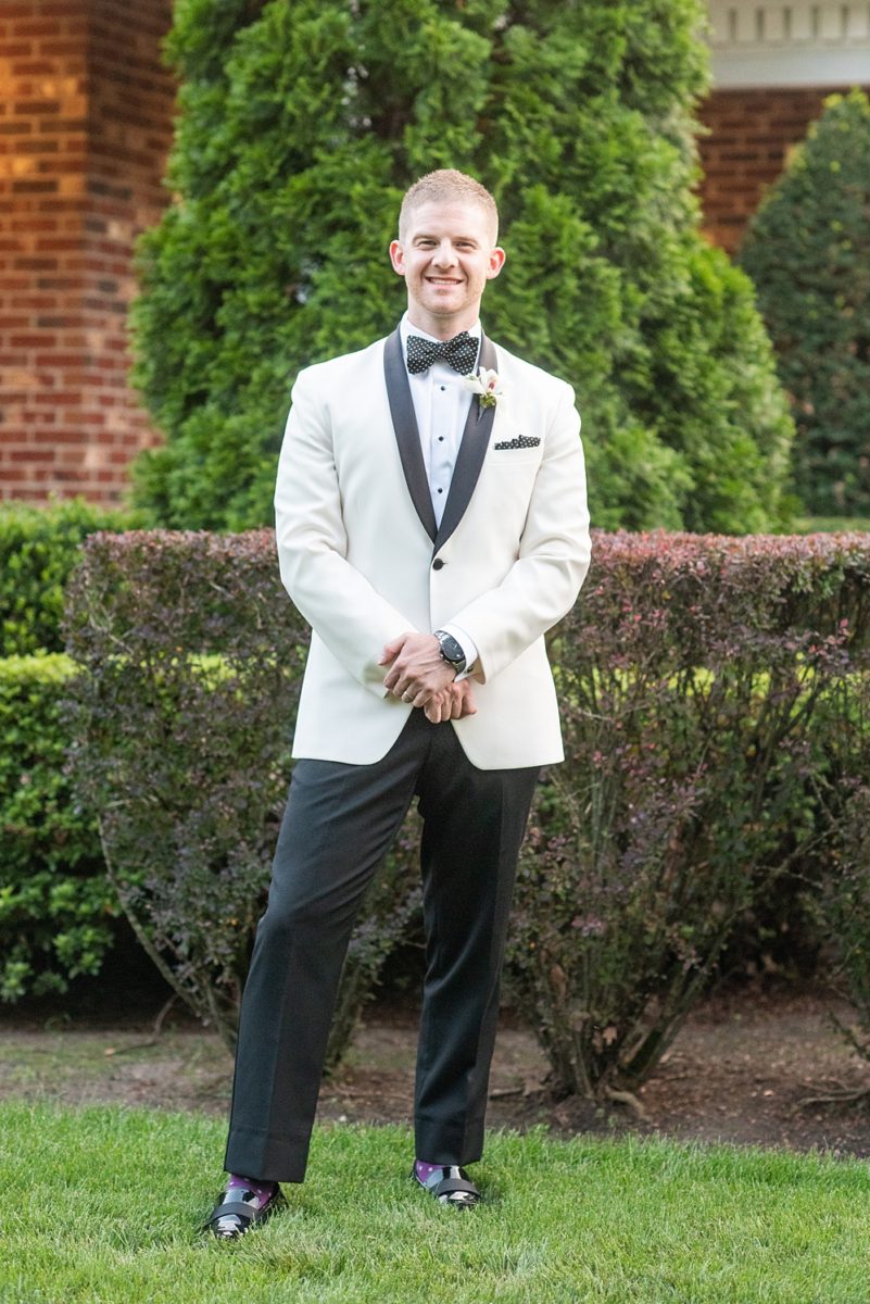 Photos of the groom's white tuxedo with black lapel and orchid boutonniere on Long Island by Mikkel Paige Photography for her East Wind wedding in Wading River, NY. The wedding venue has a beautiful outdoor ceremony area and pretty indoor reception space. #mikkelpaige #newyorkweddingphotographer #longislandweddingvenue #summer #weddingdetails #whitetuxedo #groomstyle