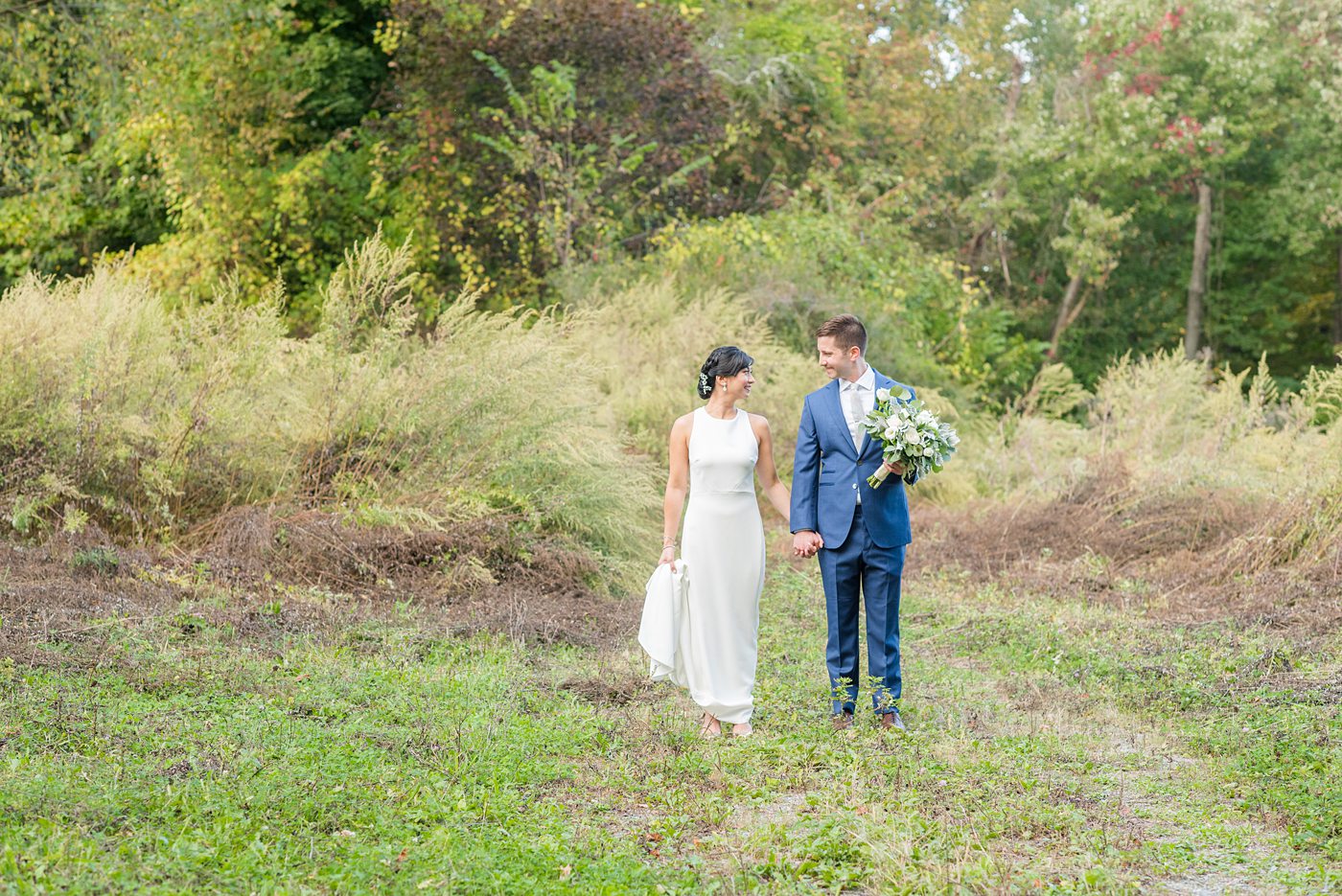 The bride and groom at their Crabtree's Kittle House wedding with an outdoor ceremony and indoor reception in Chappaqua, New York. Photos by Mikkel Paige Photography. This venue in Westchester County is near the Hudson Valley and NYC. She wore an elegant, form-fitting white gown with open back. He wore a blue suit, gray tie and rose boutonniere. #mikkelpaige #hudsonvalleyweddings #crabtreeskittlehouse #fallwedding #westchestervenues #bridestyle #elegantbride #groomstyle #filipinobride