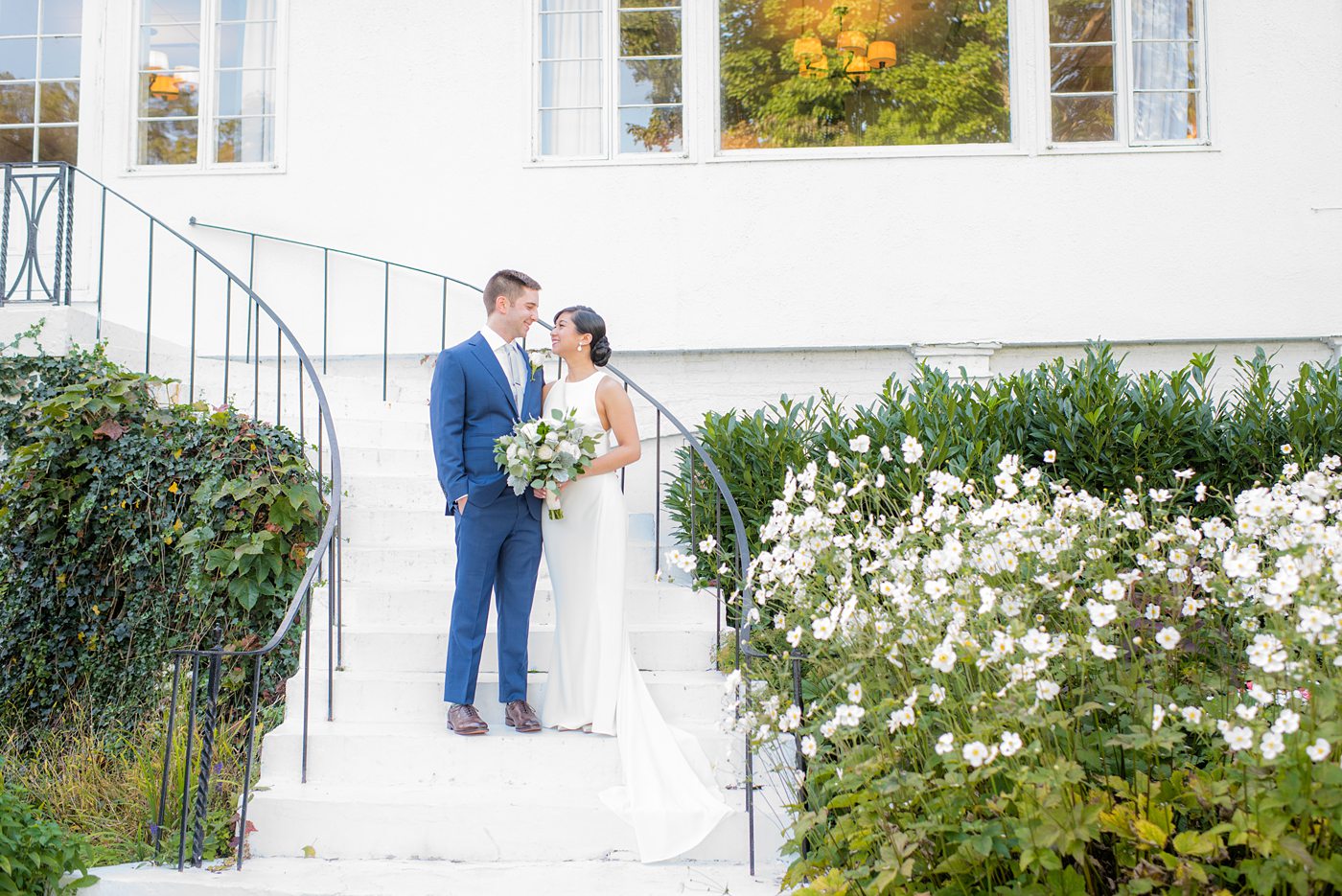 The bride and groom at their Crabtree's Kittle House wedding with an outdoor ceremony and indoor reception in Chappaqua, New York. Photos by Mikkel Paige Photography. This venue in Westchester County is near the Hudson Valley and NYC. She wore an elegant, form-fitting white gown with open back. He wore a blue suit, gray tie and rose boutonniere. #mikkelpaige #hudsonvalleyweddings #crabtreeskittlehouse #fallwedding #westchestervenues #bridestyle #elegantbride #groomstyle #filipinobride