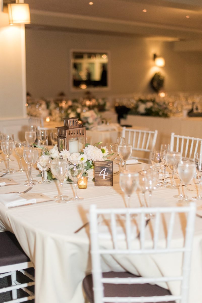 Indoor reception at Crabtree's Kittle House wedding after an outdoor ceremony in Chappaqua, New York. Table photos with lanterns and white dahlia and rose centerpieces by Mikkel Paige Photography with wood table numbers. This venue in Westchester County is near the Hudson Valley and NYC. #mikkelpaige #hudsonvalleyweddings #crabtreeskittlehouse #fallwedding #westchestervenues #reception #dahlias #centerpieces #woodtablenumbers