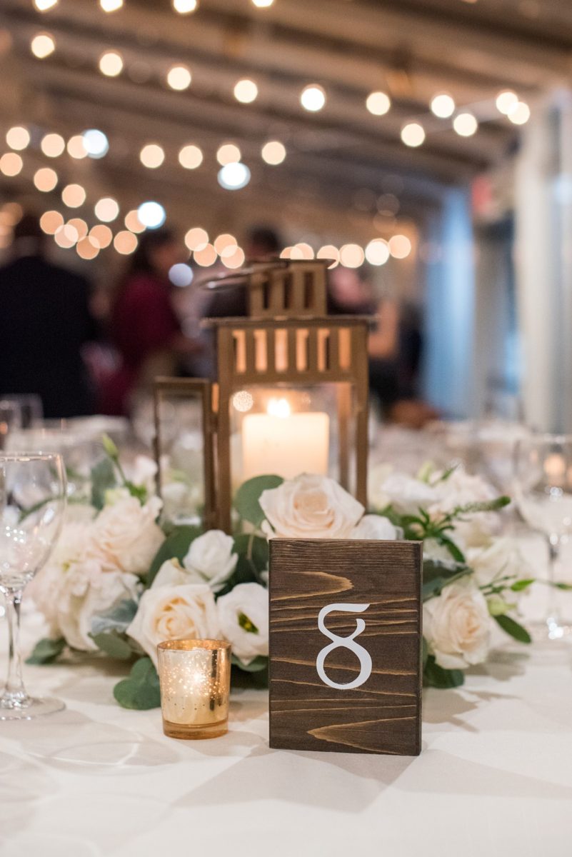 Indoor reception at Crabtree's Kittle House wedding after an outdoor ceremony in Chappaqua, New York. Table photos with lanterns and white dahlia and rose centerpieces by Mikkel Paige Photography with wood table numbers. This venue in Westchester County is near the Hudson Valley and NYC. #mikkelpaige #hudsonvalleyweddings #crabtreeskittlehouse #fallwedding #westchestervenues #reception #dahlias #centerpieces #woodtablenumbers
