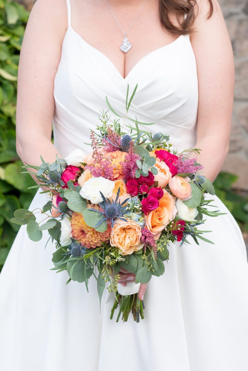 New Jersey wedding venue, Crystal Springs Resort, in Hamburg with an outdoor ceremony option and indoor reception. This detail photo of the bride's bouquet is by Mikkel Paige Photography. It had colorful flowers including blue thistle, orange ranunculus, peach roses, green eucalyptus wax flowers and sweetheart roses. #mikkelpaige #CrystalSprings #NJweddingvenues #NewJerseyWedding #NJweddingphotographer #bouquet #fallbouquet #autumnbouquet #colorfulbouquet #detailshots #detailphotos