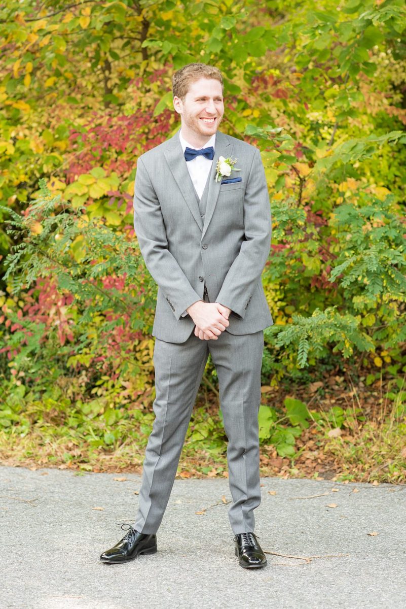 Groom dressed in a grey suit for a fall wedding in upstate New York, just outside NYC, in Chappaqua, Westchester County. The wedding at Crabtree's Kittle House had an outdoor ceremony then reception indoors. It was filled with pumpkins, autumn leaves, orange, white, and peach colors. Detail white boutonniere photo taken by Mikkel Paige Photography. #mikkelpaige #fallwedding #newyorkweddingvenues #nycweddingphotographer #outdoorceremony #autumnwedding #boutonnieres #ranunculus #groomstyle