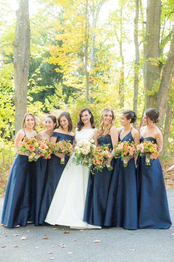 Bridal party dressed in navy blue bridesmaids gowns for a fall wedding in upstate New York, just outside NYC, in Chappaqua, Westchester County. Photos taken by Mikkel Paige Photography for a wedding at Crabtree's Kittle House. It had an outdoor ceremony and reception indoors, filled with pumpkins, autumn leaves, orange, white, and peach colors. #mikkelpaige #fallwedding #newyorkweddingvenues #nycweddingphotographer #outdoorceremony #navybluebridesmaids #autumnwedding