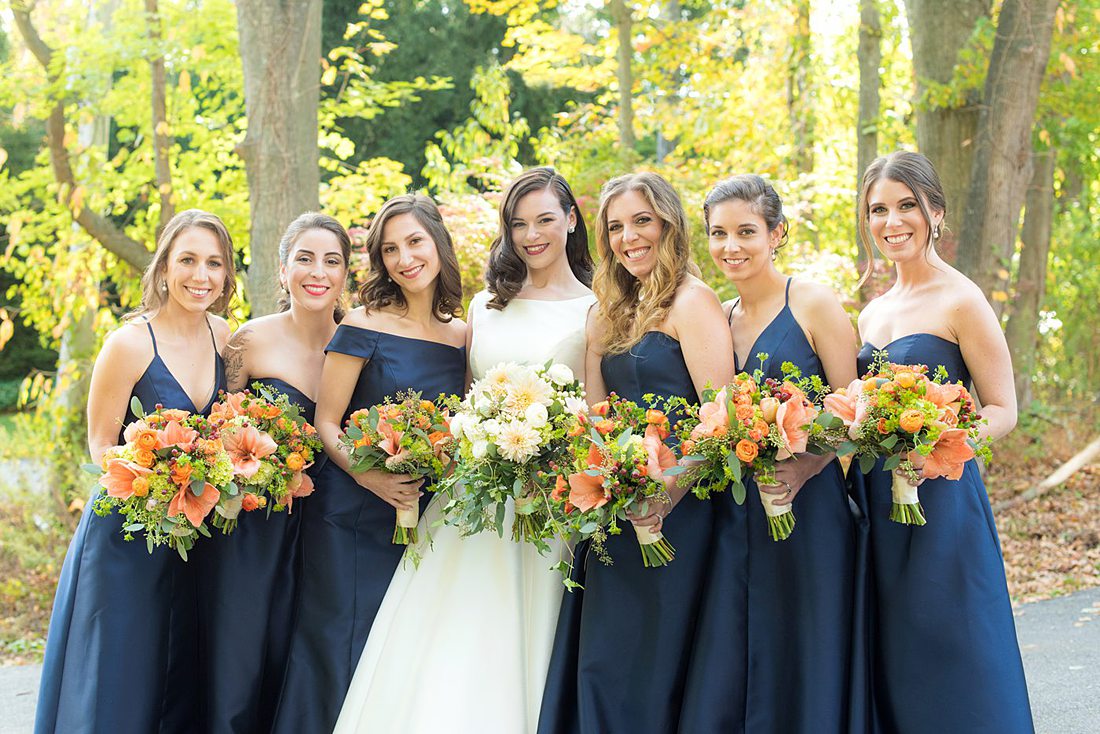Bridal party dressed in navy blue bridesmaids gowns for a fall wedding in upstate New York, just outside NYC, in Chappaqua, Westchester County. Photos taken by Mikkel Paige Photography for a wedding at Crabtree's Kittle House. It had an outdoor ceremony and reception indoors, filled with pumpkins, autumn leaves, orange, white, and peach colors. #mikkelpaige #fallwedding #newyorkweddingvenues #nycweddingphotographer #outdoorceremony #navybluebridesmaids #autumnwedding