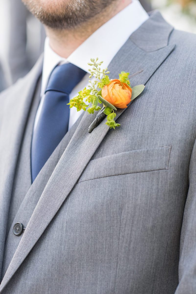 Groomsman dressed in grey suits for a fall wedding in upstate New York, just outside NYC, in Chappaqua, Westchester County. The wedding at Crabtree's Kittle House had an outdoor ceremony then reception indoors. It was filled with pumpkins, autumn leaves, orange, white, and peach colors. Detail orange boutonniere photo taken by Mikkel Paige Photography. #mikkelpaige #fallwedding #newyorkweddingvenues #nycweddingphotographer #outdoorceremony #greygroomsmen #autumnwedding #boutonnieres #ranunculus #groomstyle