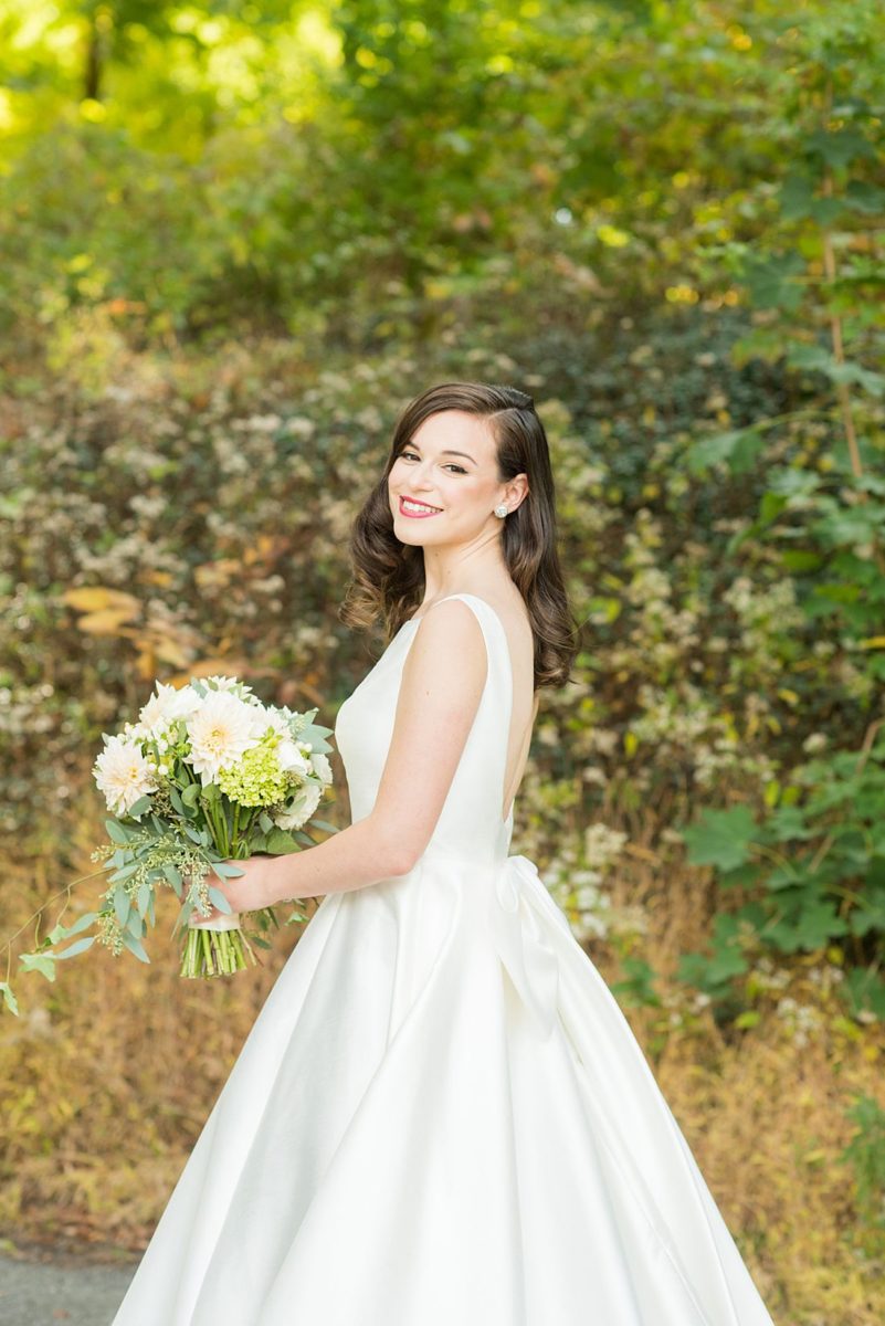 Photographs were taken by Mikkel Paige Photography for a fall wedding in upstate New York, just outside NYC, in Chappaqua, Westchester County. The bride wore a long silk gown with a bow on the back for her Crabtree's Kittle House celebration outdoors. It was filled with pumpkins, autumn leaves, orange, white, peach and navy colors. The bride's gown had a long train and back bow. #mikkelpaige #fallwedding #newyorkweddingvenues #BrideStyle #autumnbouquet #glambride #elegantbride