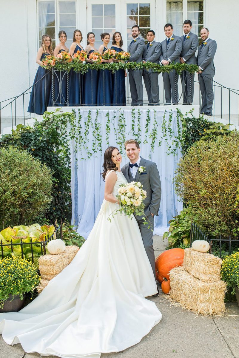 Bridal party dressed in navy blue bridesmaids gowns and grey suits for a fall wedding in upstate New York, just outside NYC, in Chappaqua, Westchester County. The wedding at Crabtree's Kittle House had an outdoor ceremony then reception indoors. It was filled with pumpkins, autumn leaves, orange, white, and peach colors. Photos taken by Mikkel Paige Photography. #mikkelpaige #fallwedding #newyorkweddingvenues #nycweddingphotographer #outdoorceremony #navybluebridesmaids #autumnwedding