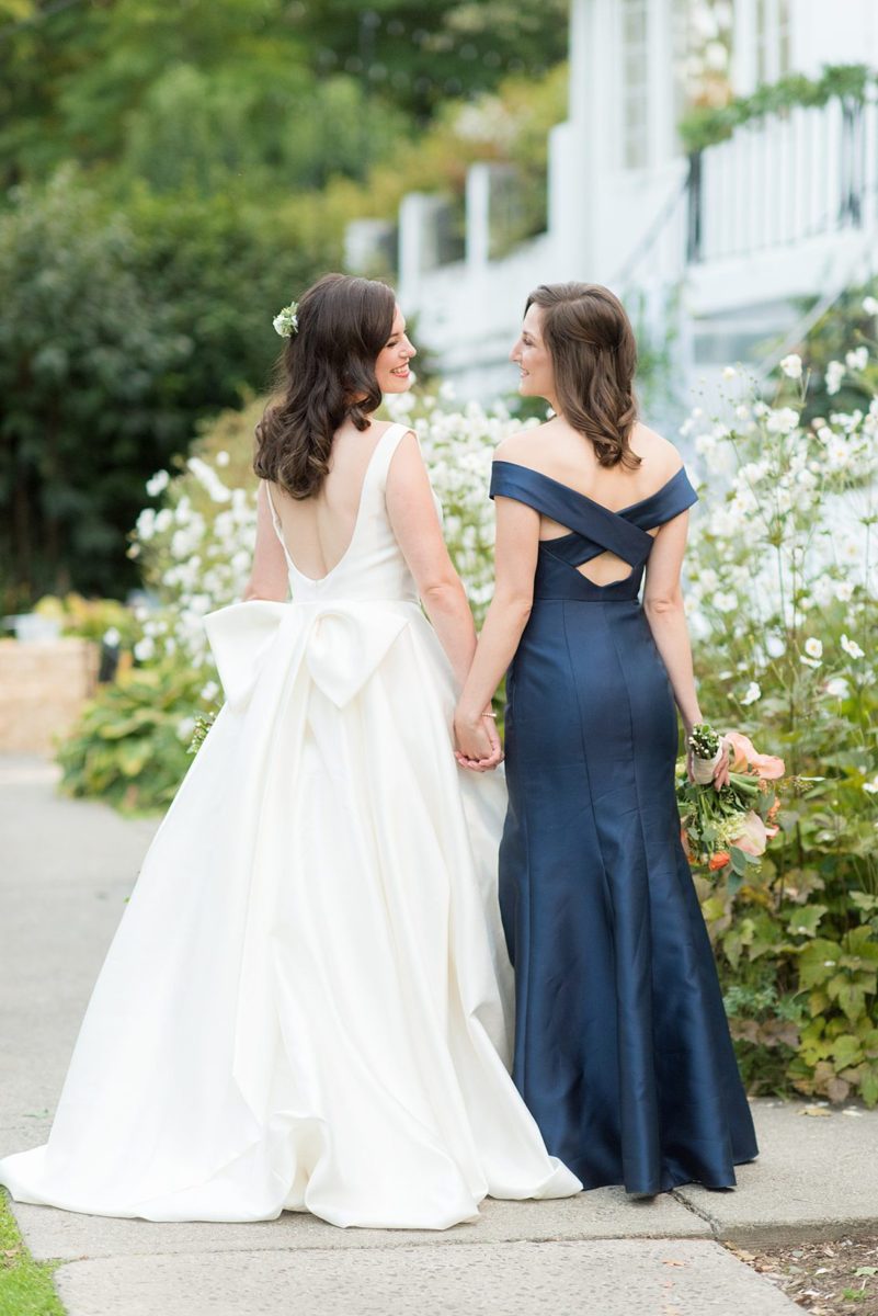 Bride dressed in a white gown with long train for her fall wedding in upstate New York, just outside NYC, in Chappaqua, Westchester County with her maid of honor in navy blue. The wedding at Crabtree's Kittle House had an outdoor ceremony and reception indoors. It was filled with pumpkins, autumn leaves, orange, white, and peach colors. Photo by Mikkel Paige Photography. #mikkelpaige #fallwedding #newyorkweddingvenues #nycweddingphotographer #bridestyle #autumnwedding #fallbouquets #MaidofHonor