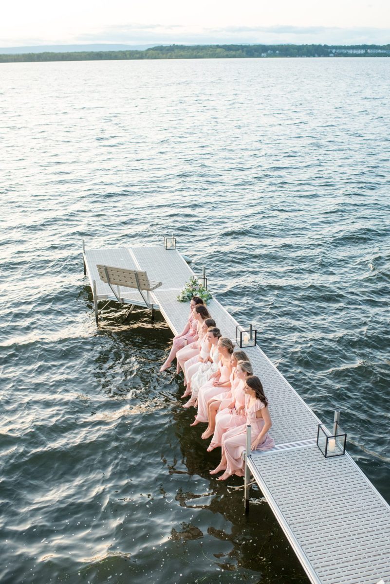 Saratoga Springs destination wedding photos in upstate New York by Mikkel Paige Photography, NY wedding photographer. The bride wore a boho lace gown and bridesmaids pink gown. They sat on the dock at the lake for a playful bridal party picture. #mikkelpaige #saratogaspringswedding #destinationwedding #bridestyle #bridalparty #weddingparty #lakefrontwedding #lakewedding