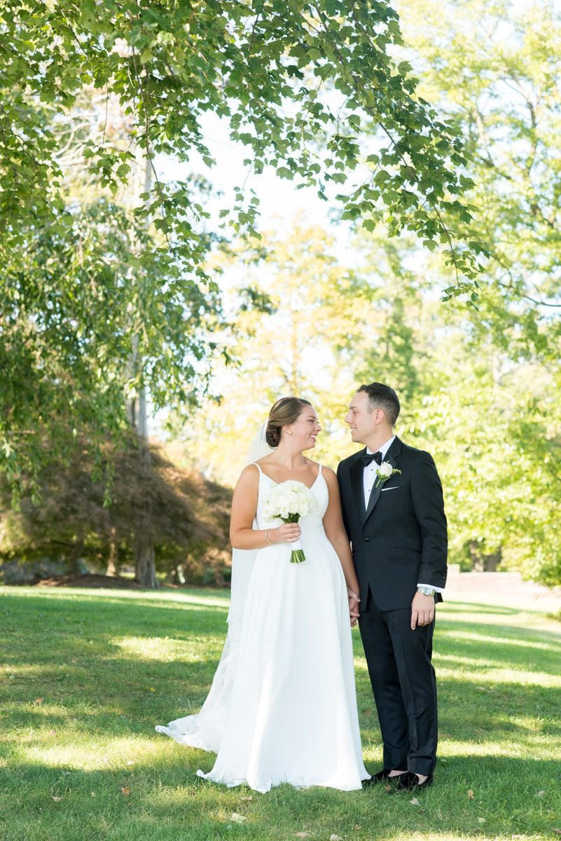 Photos by Mikkel Paige Photography at Waveny House wedding venue in New Canaan, Connecticut. This beautiful venue has an outdoor garden for the ceremony and indoor historic home for the reception. The bride and groom took photos on the park property, him in a tuxedo and her in a simple white gown with elaborate lace back. She carried an all white and ivory bouquet. #mikkelpaige #wavenyhouse #wavenyhousewedding #connecticutweddingvenue #connecticutweddingphotographer #brideandgroom #whitebouquet