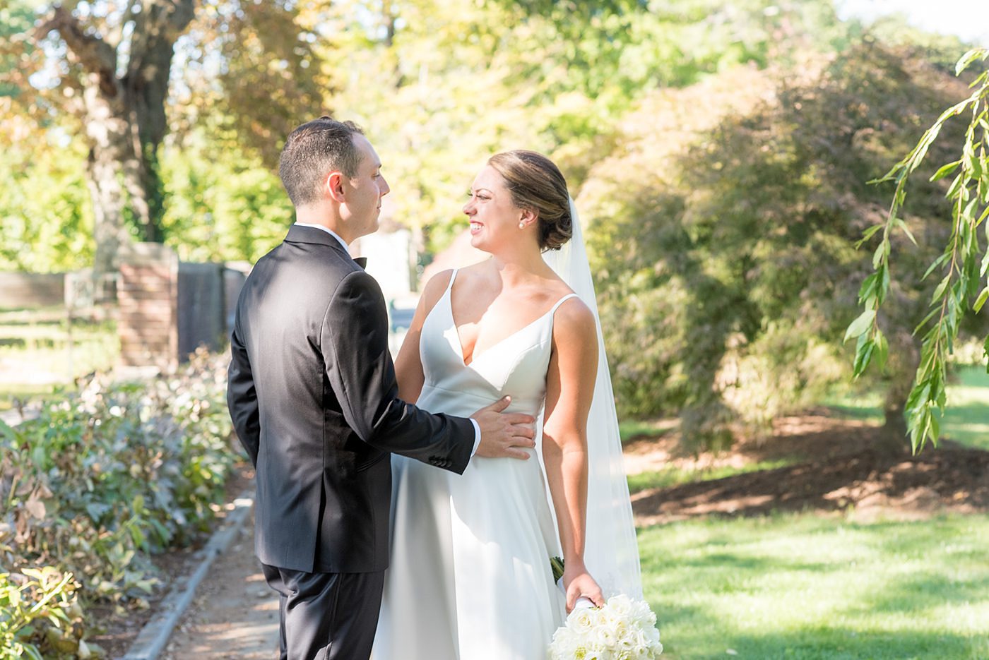 Photos by Mikkel Paige Photography at Waveny House wedding venue in New Canaan, Connecticut. This beautiful venue has an outdoor garden for the ceremony and indoor historic home for the reception. The bride and groom took photos on the park property, him in a tuxedo and her in a simple white gown with elaborate lace back. She carried an all white and ivory bouquet. #mikkelpaige #wavenyhouse #wavenyhousewedding #connecticutweddingvenue #connecticutweddingphotographer #brideandgroom #whitebouquet
