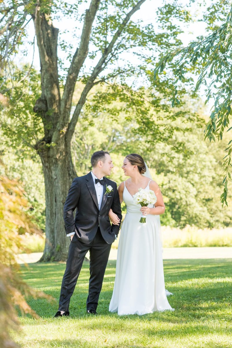 Photos by Mikkel Paige Photography at Waveny House wedding venue in New Canaan, Connecticut. This beautiful venue has an outdoor garden for the ceremony and indoor historic home for the reception. The bride and groom took photos on the park property, him in a tuxedo and her in a simple white gown with elaborate lace back. She carried an all white and ivory bouquet. #mikkelpaige #wavenyhouse #wavenyhousewedding #connecticutweddingvenue #connecticutweddingphotographer #brideandgroom #whitebouquet