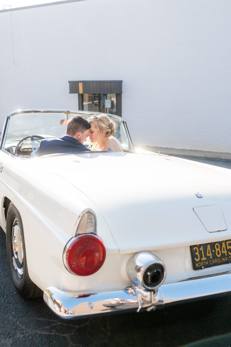 Chatham Station wedding photos by Mikkel Paige Photography from this urban chic beautiful venue in Cary, North Carolina. The bride wore a tulle v-neck gown and up hair-do with braids and groom a blue suit with custom details for a fall celebration. They took iconic photos with a vintage white Thunderbird car. #mikkelpaige #RaleighWeddingPhotographer #NorthCarolinaWeddings #SouthernWeddings #bridestyle #brideandgroom #vintagecar