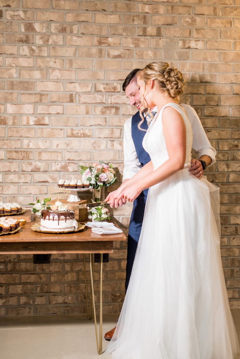 Fall photos at Cary, North Carolina wedding venue Chatham Station by Mikkel Paige Photography. This urban, beautiful space has an indoor and outdoor space near Raleigh. The bride and groom had a small chocolate covered gluten free cake with a custom name topper with mini-cupcakes surrounding it. #mikkelpaige #RaleighWeddingPhotographer #NorthCarolinaWeddings #SouthernWeddings #fallwedding #RaleighWedding #CaryNorthCarolina #weddingcake #smallweddingcake