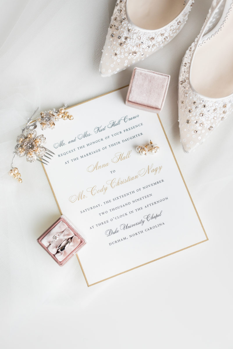 Wedding photographer Mikkel Paige Photography captures a ceremony at Duke Chapel and reception at The Rickhouse, a beautiful downtown venue in Durham, North Carolina. The bride and groom got ready at the JB Duke Hotel. Photo of details of the pearl earrings, bride's high heel shoes, classic white and gold invitation and gold rings with a pink The Mrs. Box. #durhamweddingphotographer #DukeChapelWedding #DurhamWeddingNorthCarolina #DurhamWeddingPhootgrapher #MikkelPaige #bridestyle #themrsbox