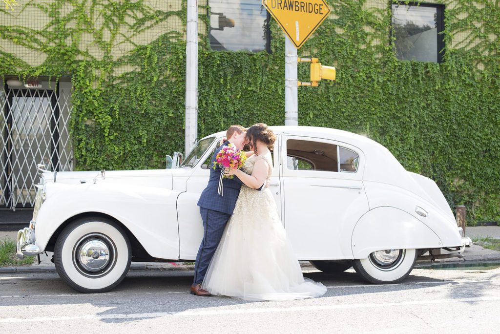 A 501 Union wedding in Brooklyn with photos by Mikkel Paige Photography. Two brides give each other affection in front of their vintage white Rolls Royce for the day.