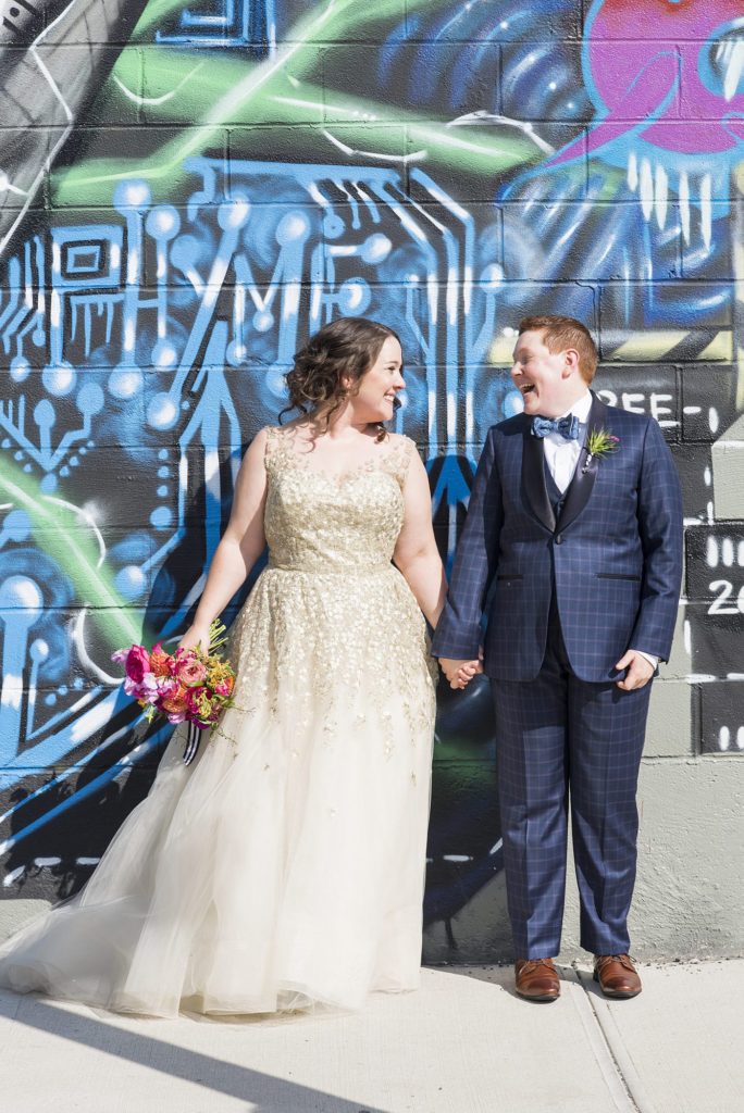 A 501 Union wedding with photos by Mikkel Paige Photography. Two brides show affection during their same sex wedding day celebration against a mural in Brooklyn, NY.