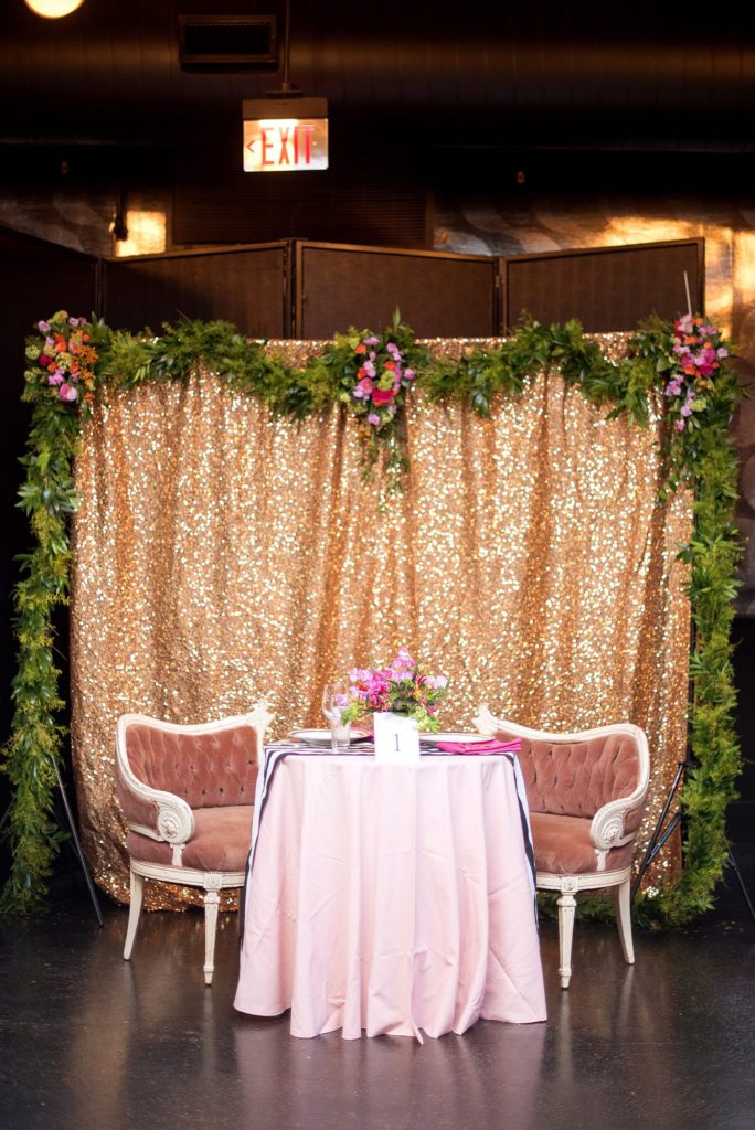 501 Union wedding with photos by Mikkel Paige Photography of the sweetheart table. Pink velvet chairs were in front of a gold sequin backdrop with green garland. Flowers by August Sage and Violet and planning by Ashley Chamblin Events.