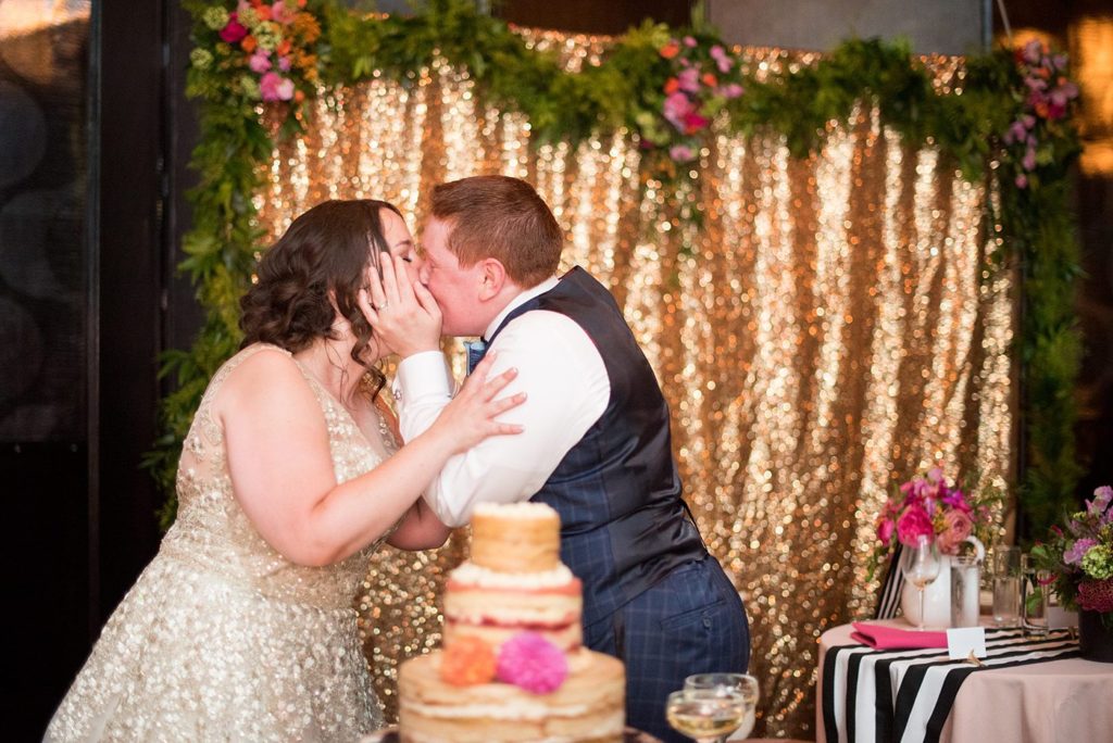 501 Union wedding with photos by Mikkel Paige Photography. The two brides kissed by their Momofuku Milk Bar cake and sequin backdrop near their sweetheart table during their reception.