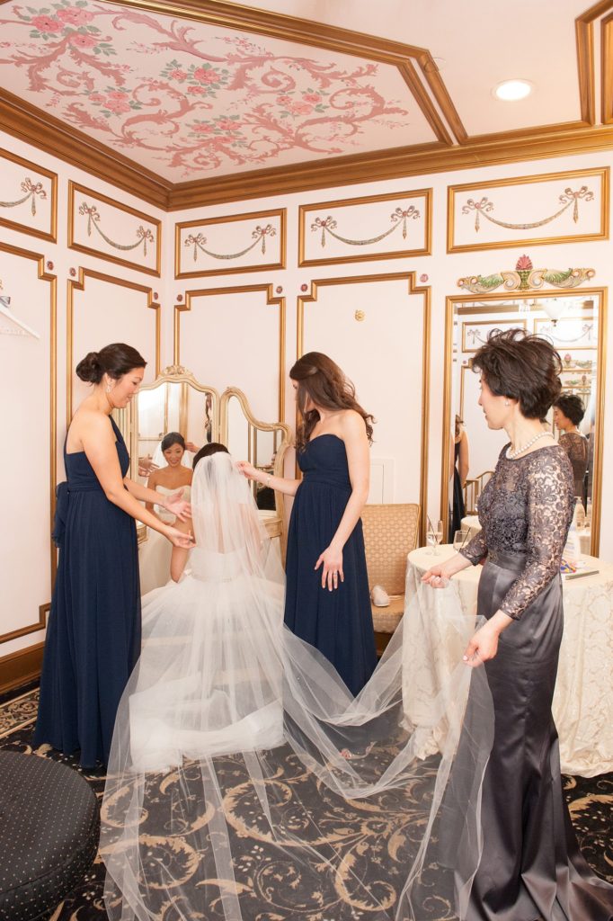 The bride's mother and bridesmaids help put her veil on at her Crystal Plaza Wedding in New Jersey with photos by Mikkel Paige Photography.