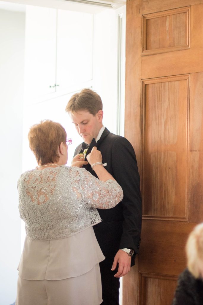 The mother of the groom helps put on his boutonniere at a summer celebration at Southwood Estate. This Hudson Valley wedding was photographed by Mikkel Paige Photography and planned by The Union Studio.