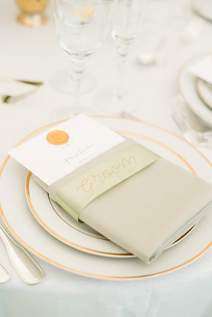 A Hudson Valley Wedding had table place settings with sage green linens and custom gold wax seals. Photos at this Southwood Estate wedding at by Mikkel Paige Photography. Planning by The Union Studio.