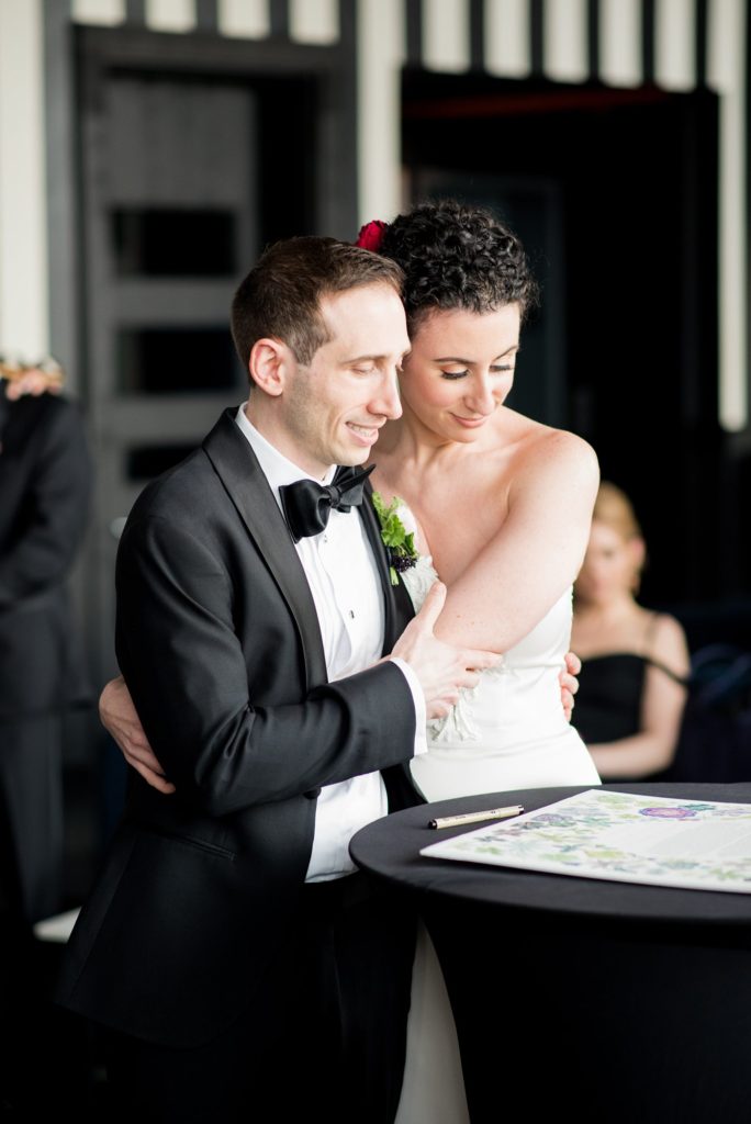 Photos of the bride and groom signing their ketubah at their W Hoboken Wedding by Mikkel Paige Photography. Floral design by Sachi Rose.