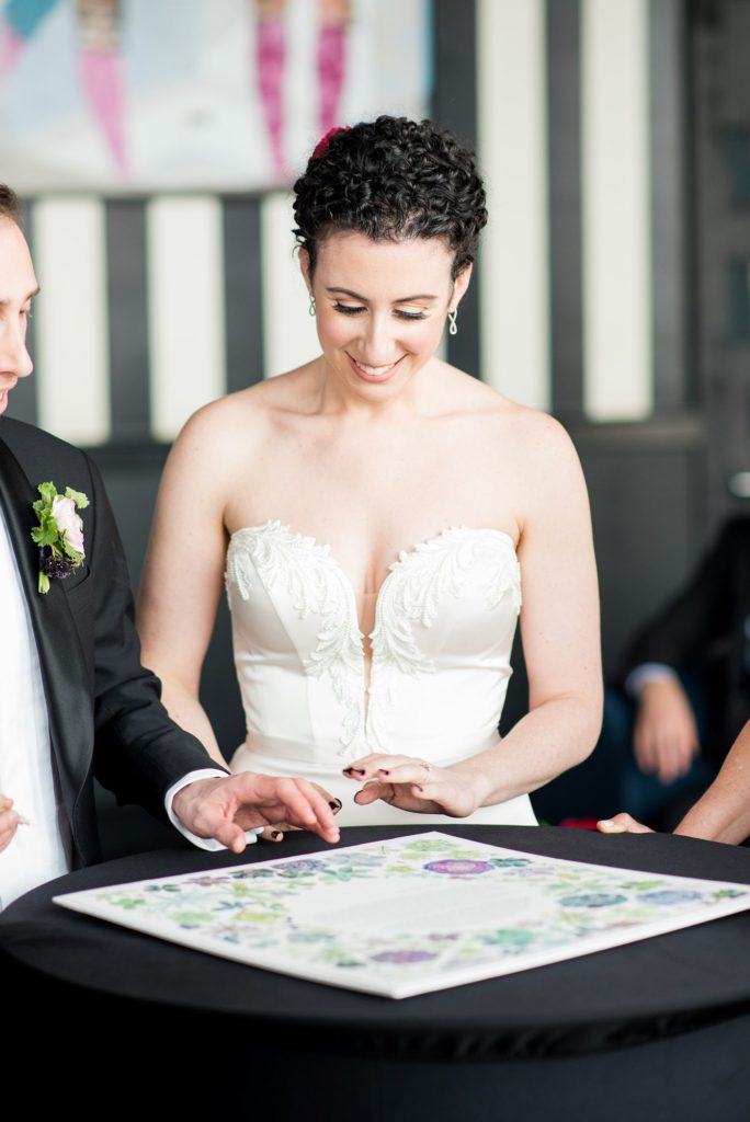 Photos of the bride and groom signing their ketubah at their W Hoboken Wedding by Mikkel Paige Photography. Floral design by Sachi Rose.