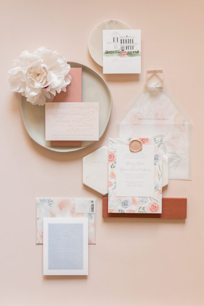 Invitation with peach flowers in a flat lay photo with a big peony in the top left and various invitation details.