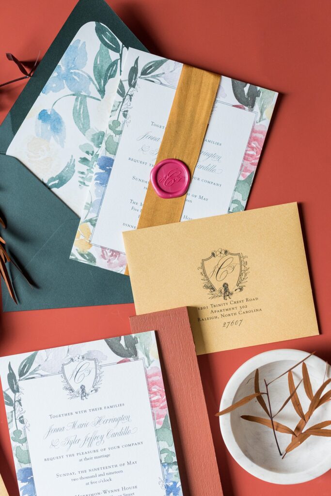Flat lay photo of a stationery set with various paper elements and a red wax seal on a mustard-yellow colored silk ribbon on the invitation.