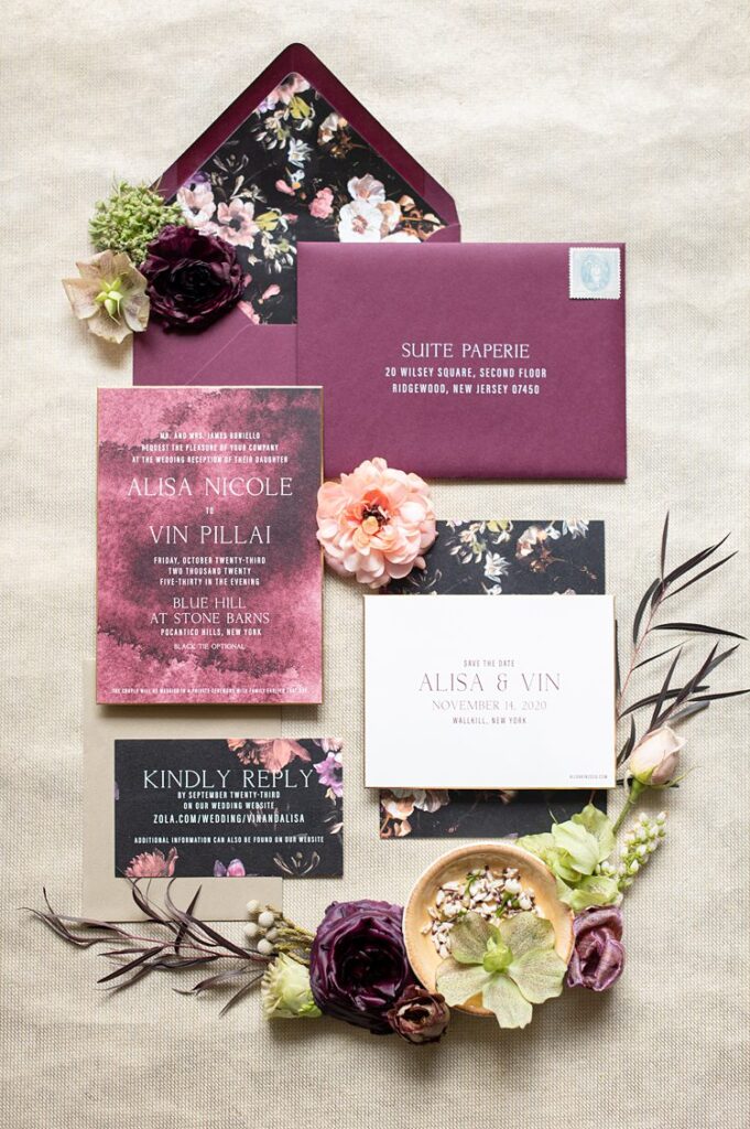 Wedding stationery with wine colored paper and floral details against a black background.
