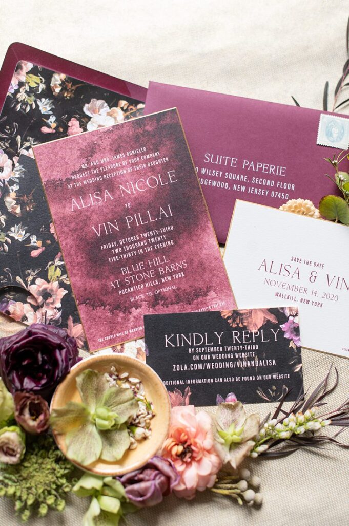 Wedding stationery with wine colored paper and floral details against a black background.