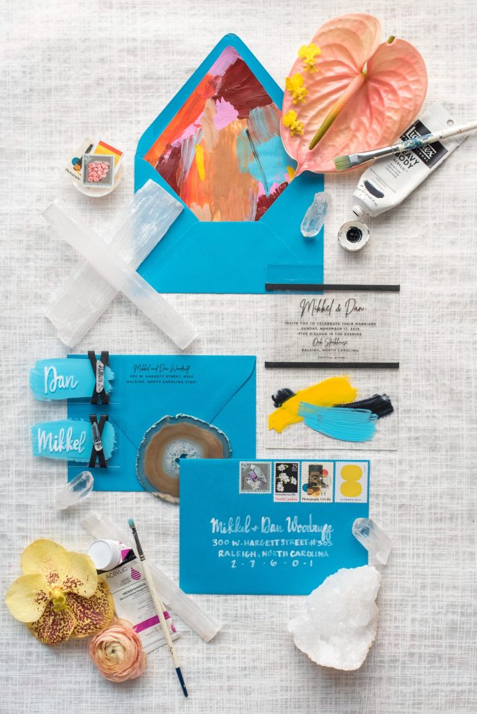 Flat lay styled photo by Mikkel Paige Photography of a bright blue invitation with gemstone for her own intimate elopement wedding in downtown Raleigh, North Carolina.