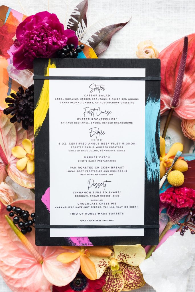 Flat lay styled photo by Mikkel Paige Photography of a menu with bright flowers for her own intimate elopement wedding in downtown Raleigh, North Carolina.