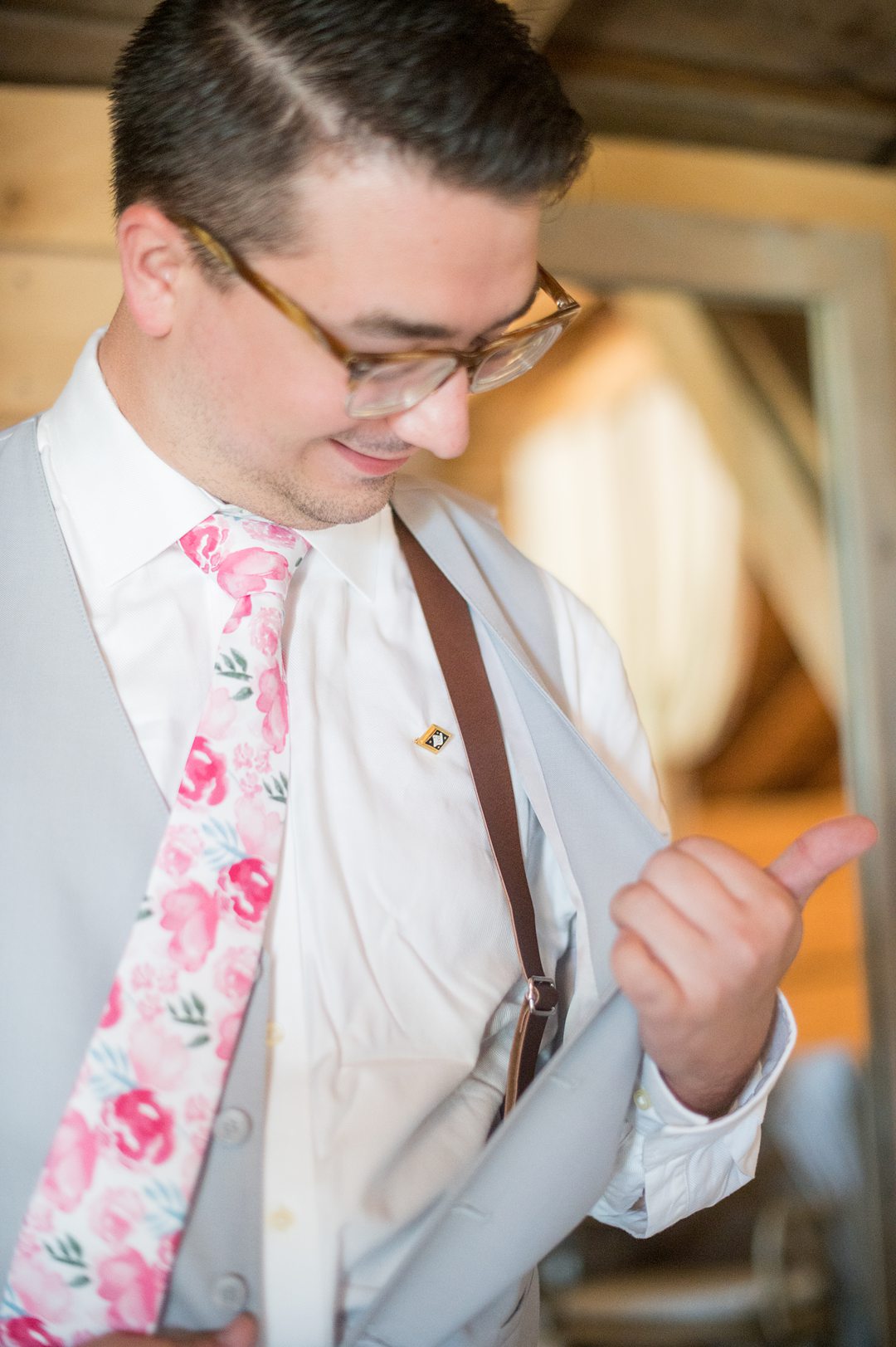 Groom in a grey suit with a pink floral tie and pocket square, and brown leather suspenders, for a small wedding in Charlottesville, VA during COVID. Photos by Mikkel Paige Photography.