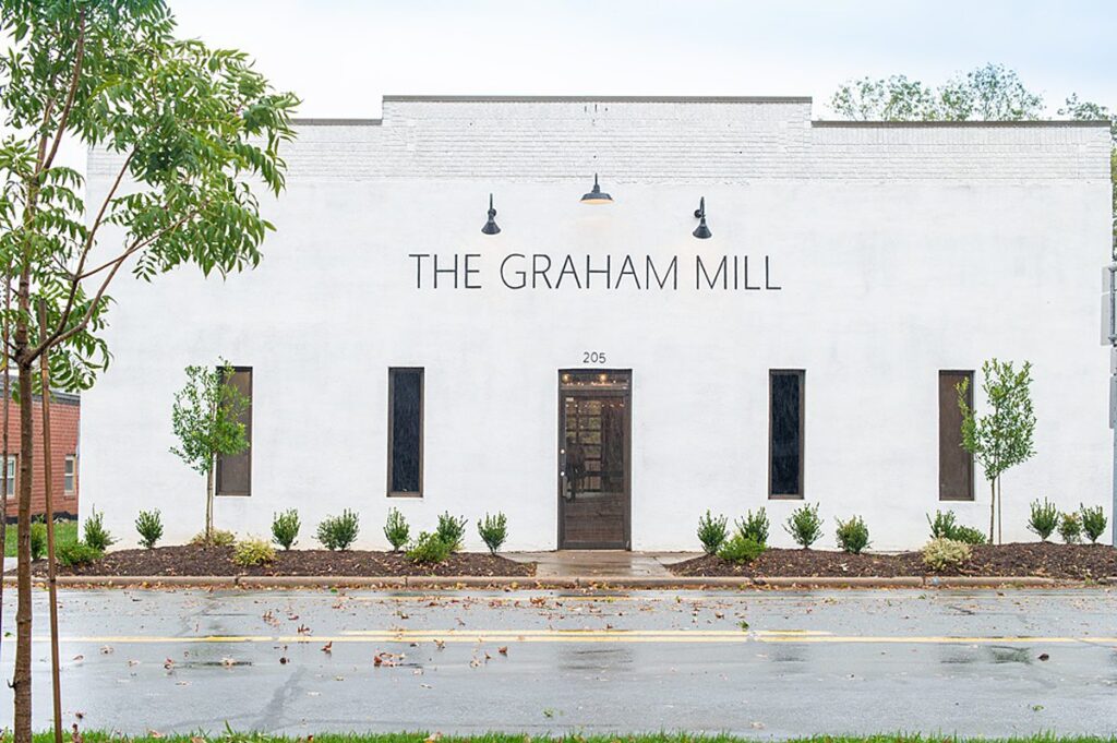 Front of a building painted in white with "The Grand Mill" painted in black letters on top.