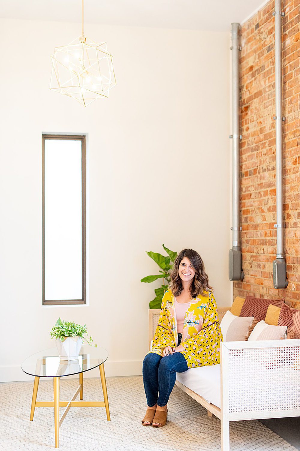 A woman in pink and yellow on a couch with a brick wall behind her and glass coffee table in front of her at The Graham Mill.