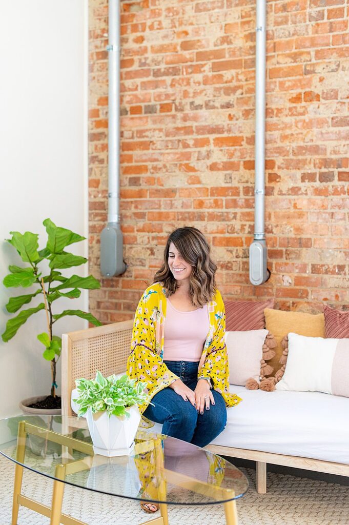 A woman in pink and yellow on a couch with a brick wall behind her at The Graham Mill wedding venue in NC.