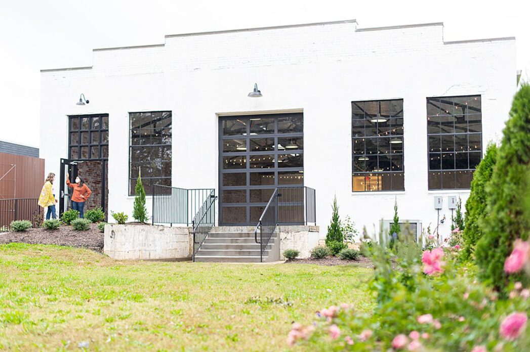 Back of The Graham Mill in NC with black large windows, white brick and a lawn with roses.