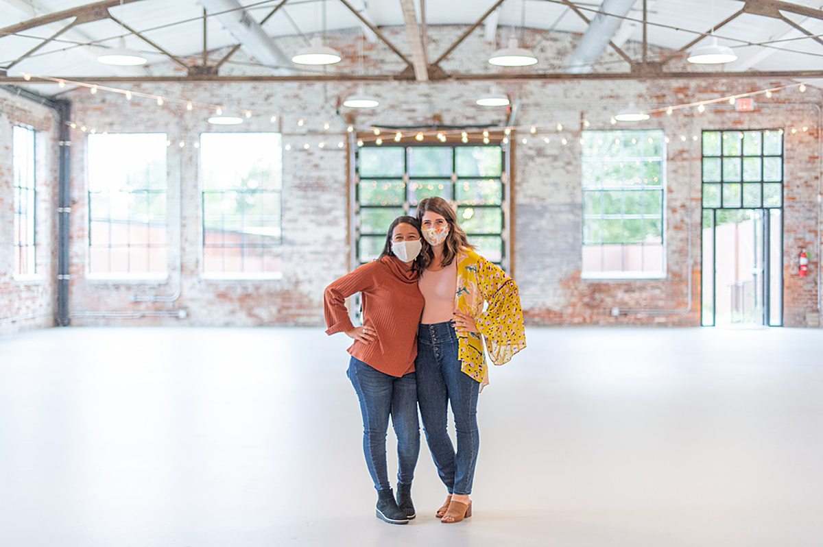 Two women with masks on inside the white brick historic Graham Mill building, a wedding venue in North Carolina.
