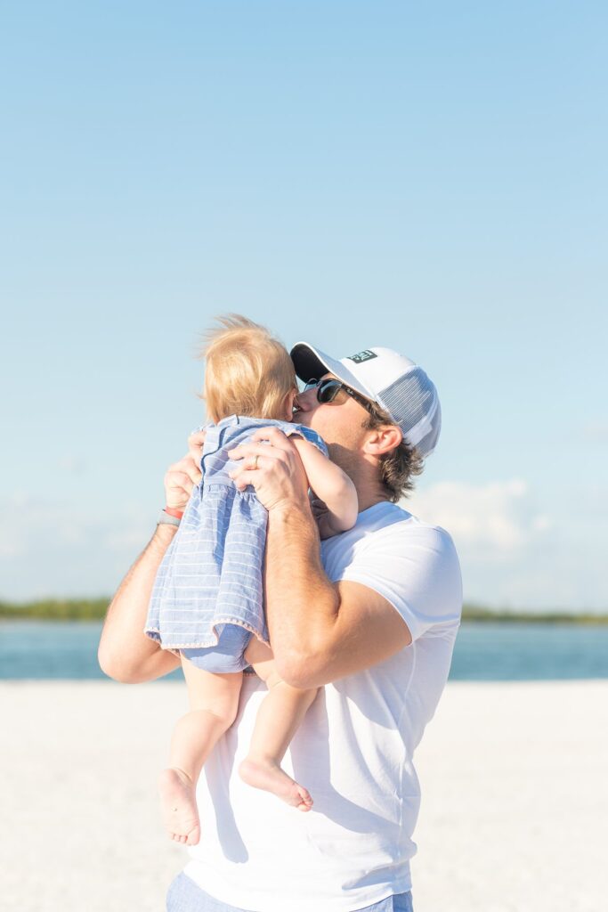 Father kissing his infant daughter on a beach in Marco Island by Mikkel Paige Photography.