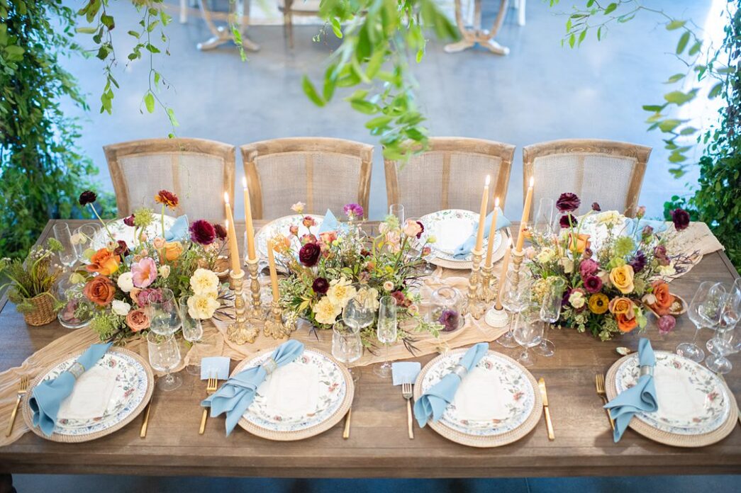 Wooden table with chairs, and plates with blue napkins under a greenery canopy at The Maxwell in NC.
