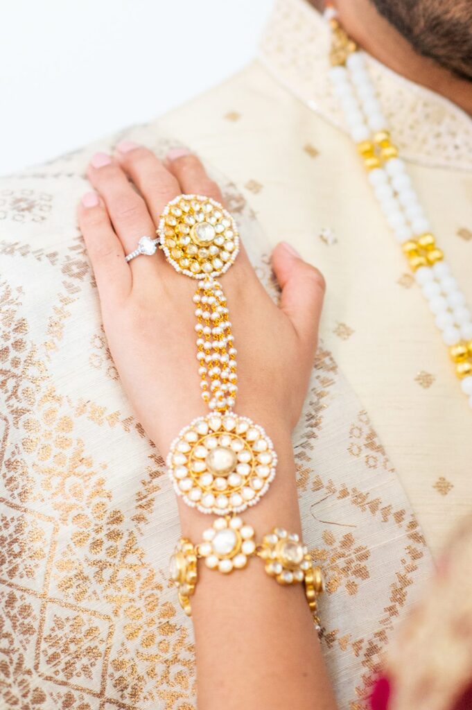 Hand with Indian wedding jewels and an oval shaped engagement ring.