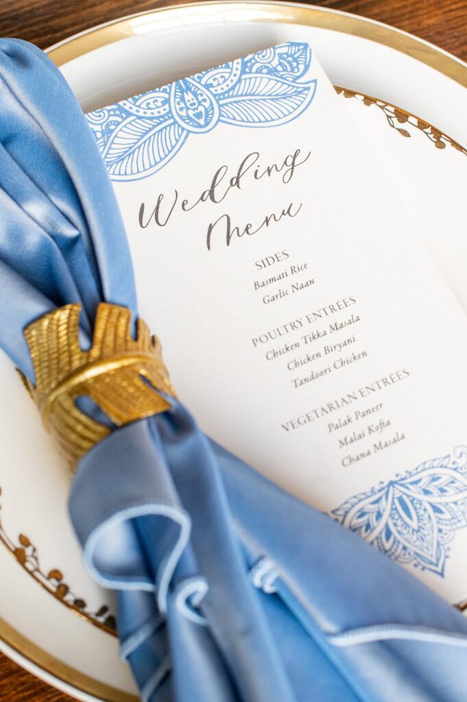 Place setting with a blue napkin and gold leaf ring next to a menu at an Indian wedding in NC.