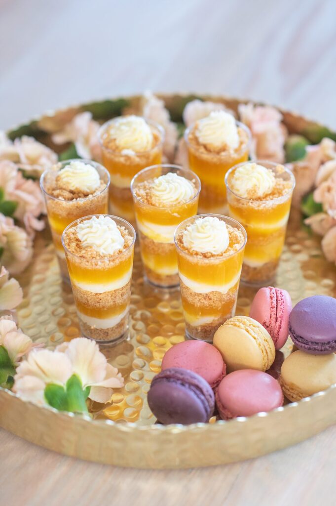 Dessert cups with whipped cream and mango layers and pink, yellow and purple macarons for an Indian wedding.
